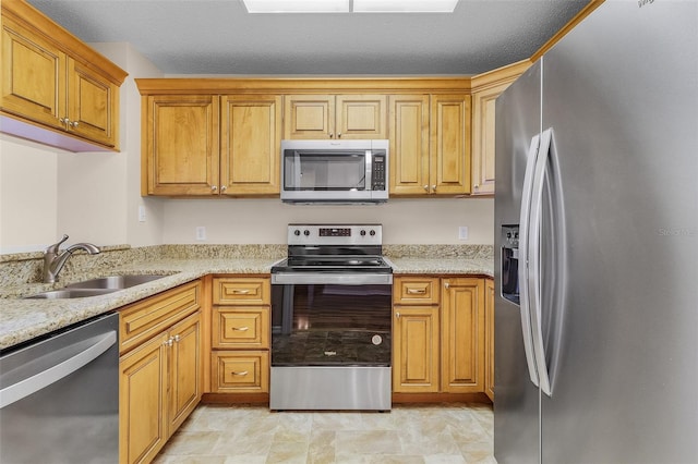 kitchen featuring appliances with stainless steel finishes, brown cabinetry, a sink, and light stone countertops