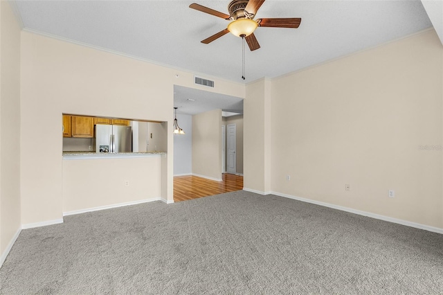 unfurnished living room with light colored carpet, ceiling fan with notable chandelier, visible vents, baseboards, and crown molding