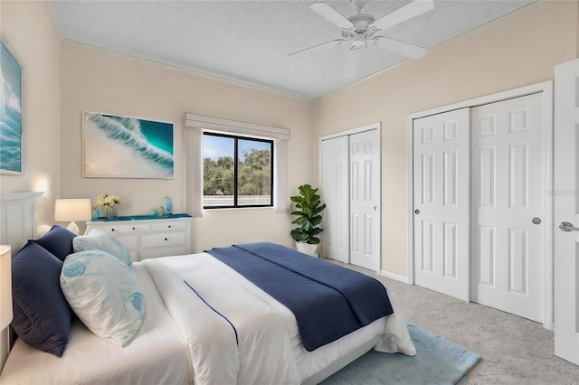 bedroom featuring light carpet, a textured ceiling, a ceiling fan, and two closets