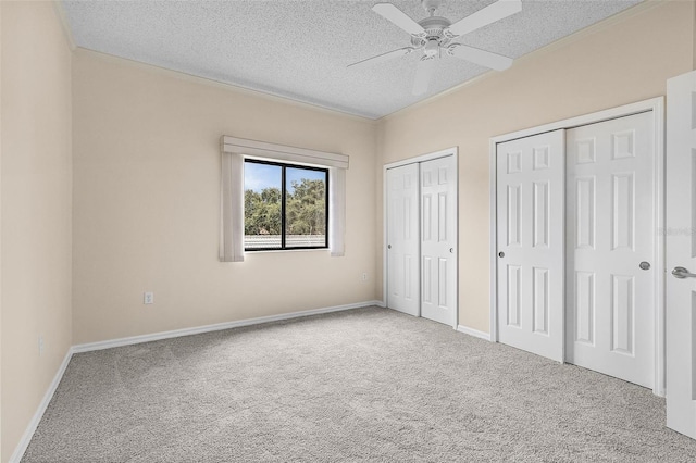 unfurnished bedroom with carpet, a textured ceiling, baseboards, and two closets