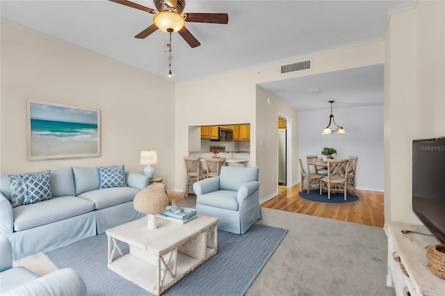 living area featuring baseboards, visible vents, a ceiling fan, light wood-style flooring, and ornamental molding