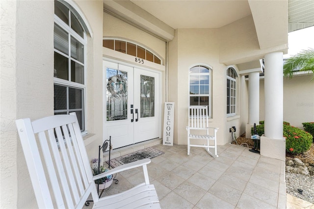 view of exterior entry featuring french doors, covered porch, and stucco siding