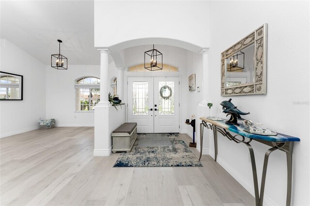 foyer featuring ornate columns, a notable chandelier, wood finished floors, and french doors