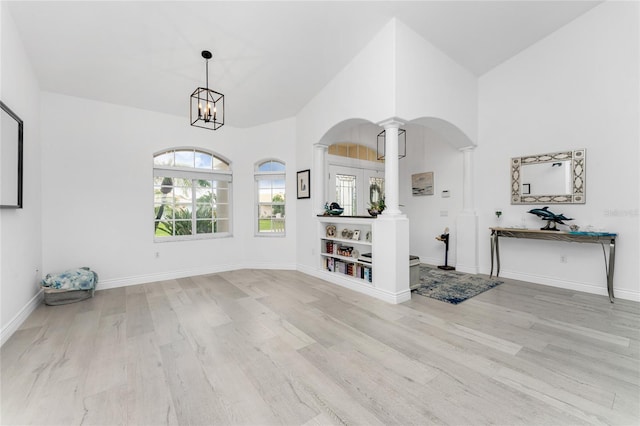 interior space featuring decorative columns, light hardwood / wood-style flooring, high vaulted ceiling, and an inviting chandelier