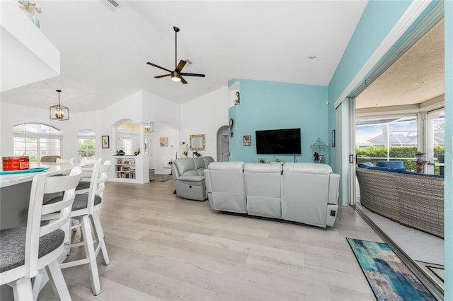 living area featuring arched walkways, vaulted ceiling, ceiling fan with notable chandelier, and light wood-style flooring