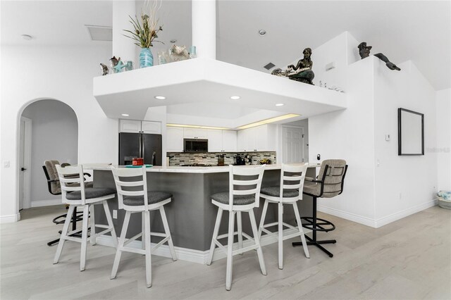 kitchen with white cabinets, black refrigerator, light wood-type flooring, and a breakfast bar area