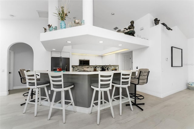 kitchen with arched walkways, decorative backsplash, stainless steel microwave, black refrigerator, and white cabinetry