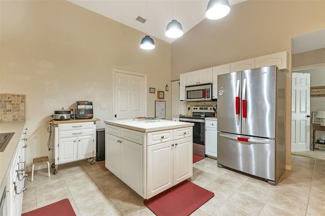 kitchen with decorative light fixtures, backsplash, a center island, stainless steel appliances, and white cabinets