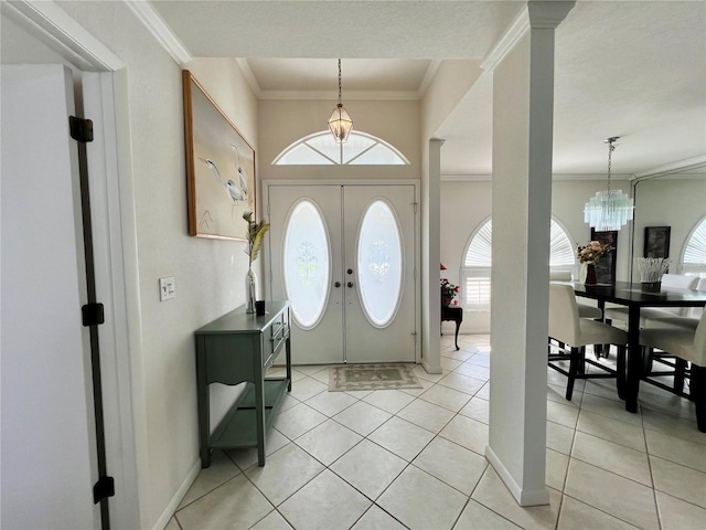 entryway with a textured ceiling, an inviting chandelier, light tile patterned floors, french doors, and crown molding