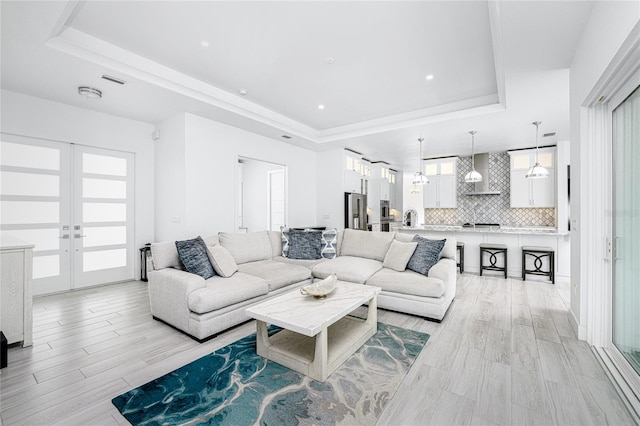 living room featuring light hardwood / wood-style floors, a raised ceiling, and french doors