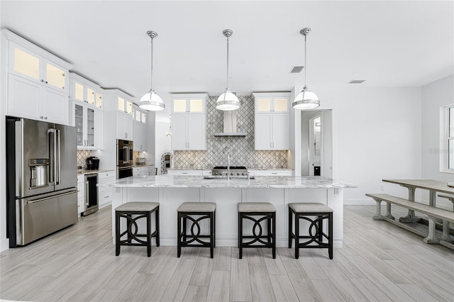 kitchen featuring light hardwood / wood-style flooring, a kitchen bar, decorative light fixtures, high end refrigerator, and a center island with sink