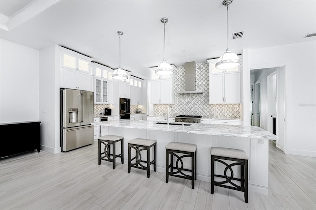 kitchen with light wood-type flooring, appliances with stainless steel finishes, a center island with sink, and wall chimney exhaust hood