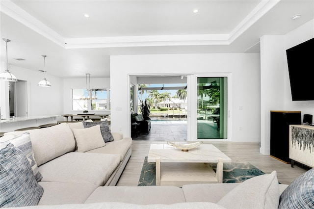 living room featuring a tray ceiling, an inviting chandelier, and light hardwood / wood-style floors