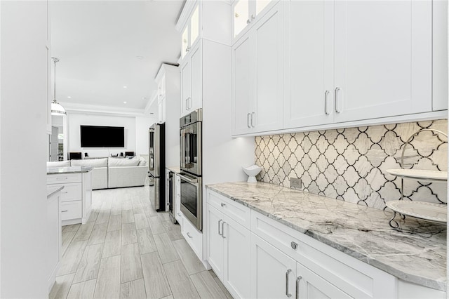 kitchen with white cabinets, light wood-type flooring, light stone counters, stainless steel appliances, and tasteful backsplash