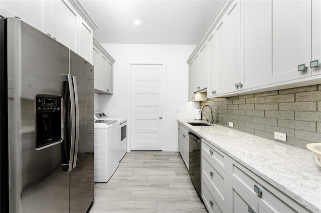 kitchen with independent washer and dryer, white cabinetry, stainless steel appliances, light stone counters, and sink