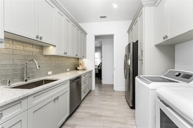 kitchen with separate washer and dryer, stainless steel appliances, sink, light stone countertops, and light hardwood / wood-style floors