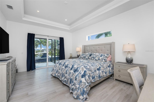 bedroom featuring light hardwood / wood-style floors, a tray ceiling, and access to outside