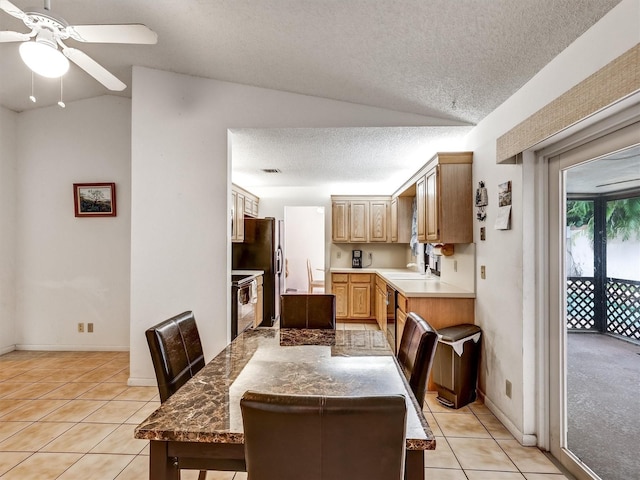 tiled dining area with a textured ceiling, ceiling fan, sink, and vaulted ceiling