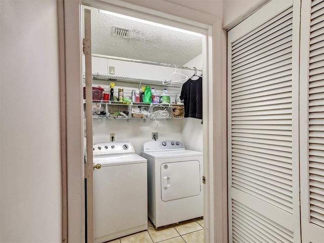 clothes washing area featuring washer and dryer, light tile patterned flooring, and a textured ceiling