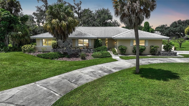 ranch-style home featuring a tile roof, a lawn, and stucco siding