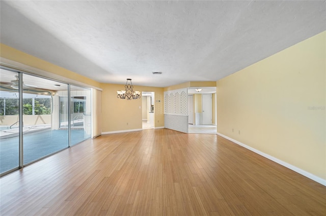 unfurnished living room featuring visible vents, baseboards, a textured ceiling, light wood-type flooring, and a notable chandelier