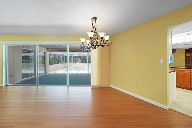 empty room with light wood-type flooring, a sunroom, baseboards, and an inviting chandelier