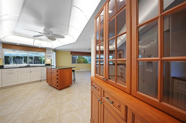 kitchen featuring a raised ceiling, dark countertops, a kitchen island, glass insert cabinets, and a sink