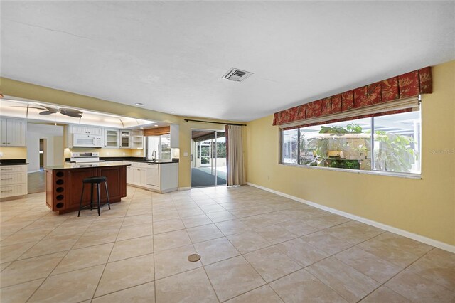 kitchen with white appliances, light tile patterned floors, a kitchen breakfast bar, a center island, and white cabinets