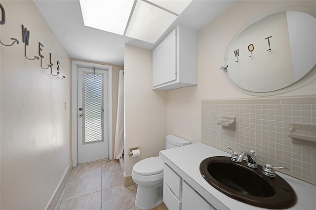 bathroom with toilet, a skylight, vanity, baseboards, and tile patterned floors