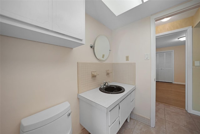 bathroom with a skylight, toilet, vanity, baseboards, and tile patterned floors