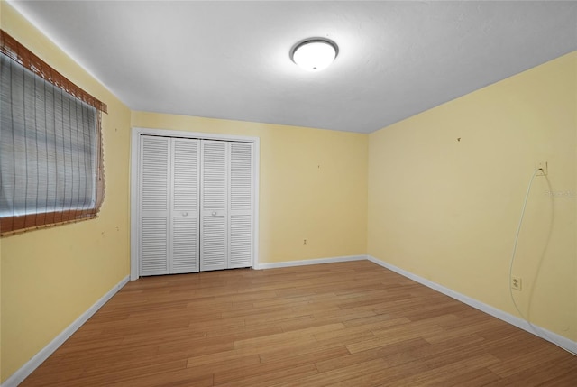 unfurnished bedroom featuring light wood finished floors, a closet, and baseboards