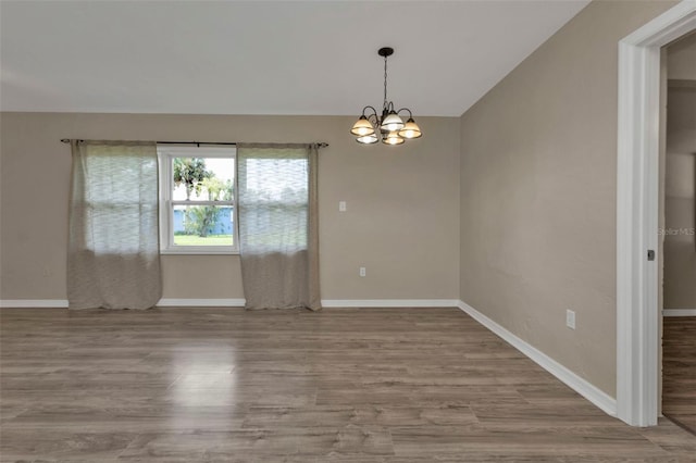 spare room with a notable chandelier, light wood-type flooring, and vaulted ceiling