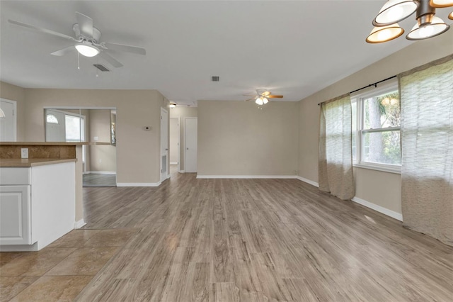 unfurnished living room featuring ceiling fan with notable chandelier and light hardwood / wood-style flooring