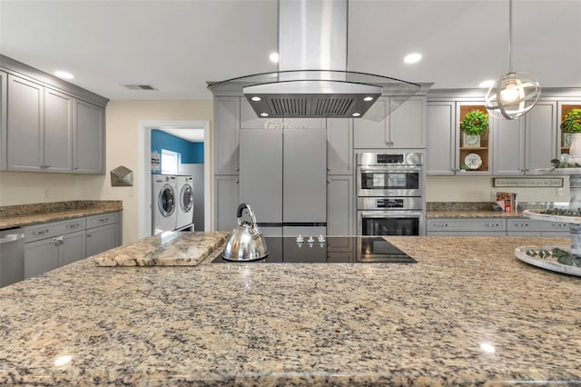 kitchen featuring light stone counters, island range hood, double oven, independent washer and dryer, and hanging light fixtures