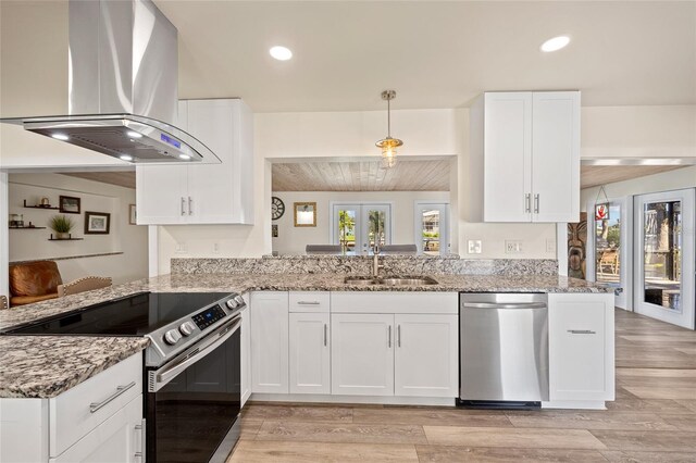 kitchen with light stone countertops, island range hood, kitchen peninsula, stainless steel appliances, and white cabinets