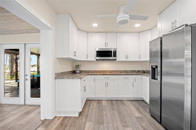 kitchen featuring light hardwood / wood-style flooring, stainless steel appliances, ceiling fan, dark stone countertops, and white cabinets