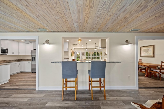 kitchen with a breakfast bar, stainless steel appliances, kitchen peninsula, white cabinetry, and light wood-type flooring