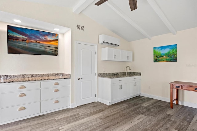 kitchen featuring a wall mounted AC, white cabinetry, lofted ceiling with beams, and light hardwood / wood-style flooring