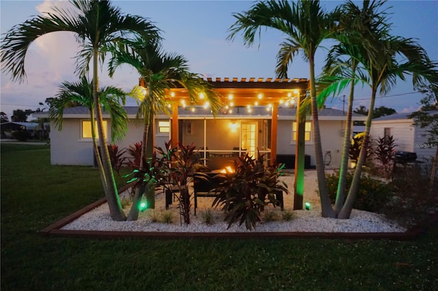 back house at dusk featuring a lawn and a patio area