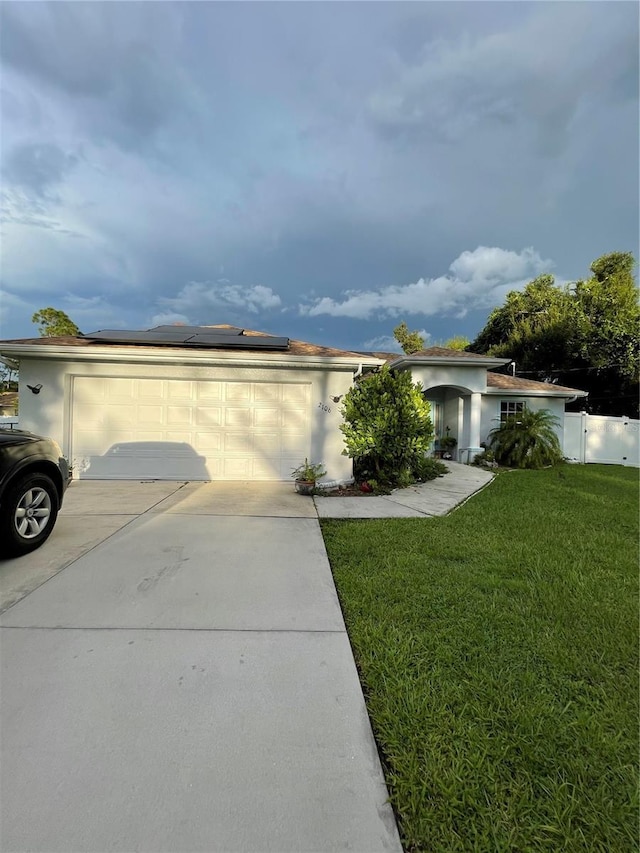 ranch-style house featuring stucco siding, concrete driveway, a front yard, roof mounted solar panels, and a garage