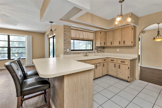 kitchen featuring light brown cabinets, light hardwood / wood-style floors, hanging light fixtures, and kitchen peninsula