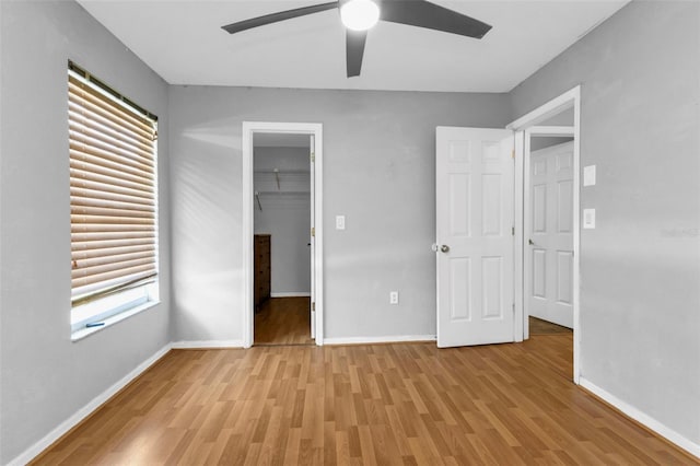 unfurnished bedroom with a spacious closet, a closet, ceiling fan, and light hardwood / wood-style flooring