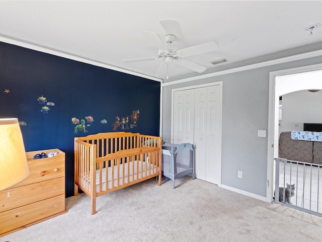 carpeted bedroom featuring a closet, ceiling fan, and a crib