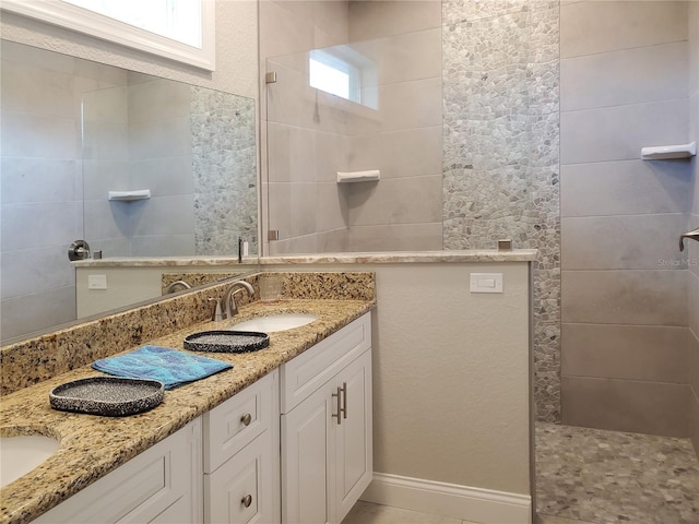 bathroom with a healthy amount of sunlight, tile patterned flooring, a tile shower, and vanity