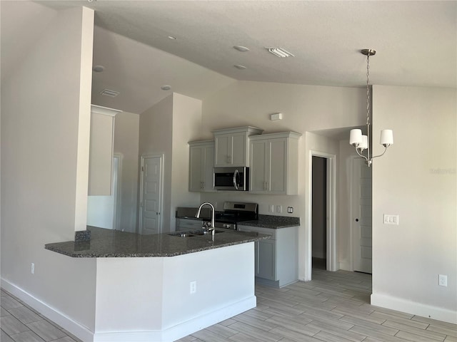 kitchen with appliances with stainless steel finishes, a peninsula, hanging light fixtures, wood finish floors, and a sink