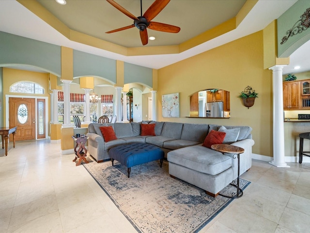 living room with decorative columns, ceiling fan with notable chandelier, and a raised ceiling