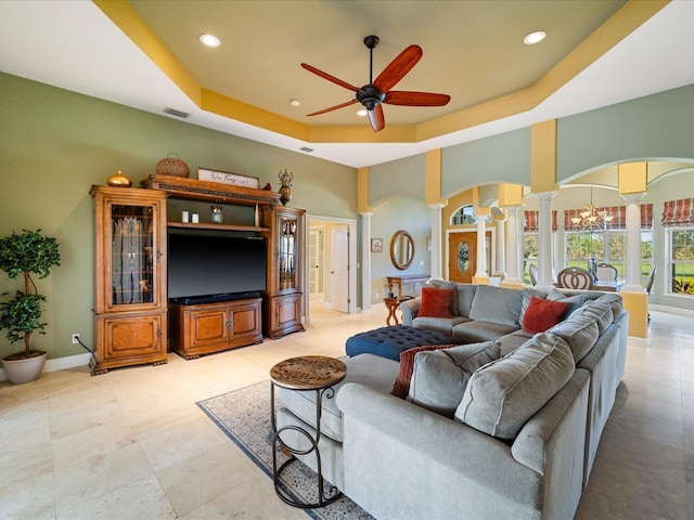 living room featuring a raised ceiling, decorative columns, and ceiling fan with notable chandelier