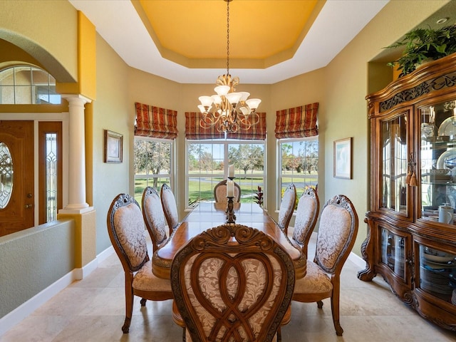 dining area featuring decorative columns, a notable chandelier, a tray ceiling, and plenty of natural light