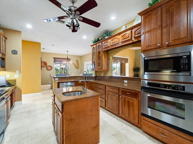 kitchen featuring an island with sink, stainless steel appliances, sink, ceiling fan with notable chandelier, and decorative light fixtures