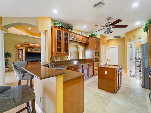 kitchen with a center island with sink, appliances with stainless steel finishes, kitchen peninsula, and ornate columns